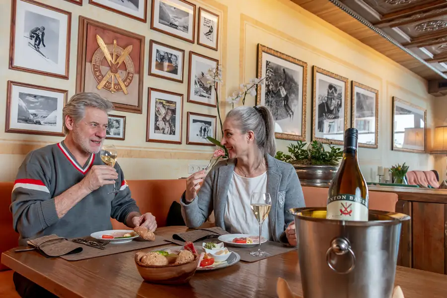 Paar mit Weißwein vor einer Wand mit historischen Skifotos