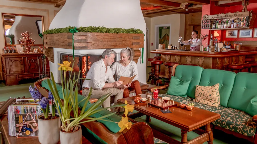 Paar liest die Karte am Kamin der Lounge, Barkeeper im Hintergrund