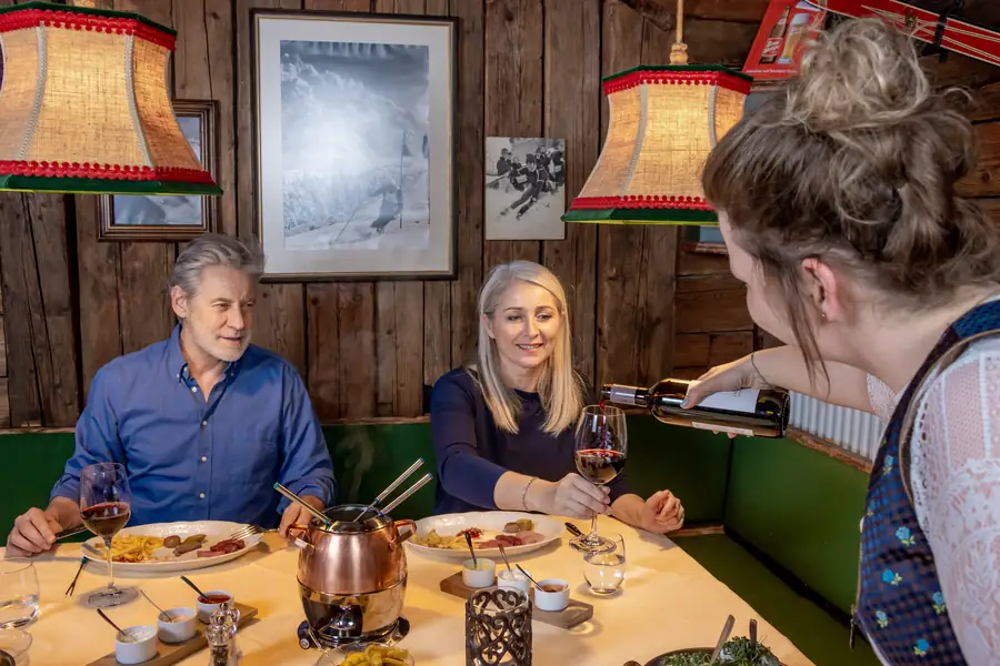 Paar beim Fondue, Servicekraft schenkt Rotwein ein