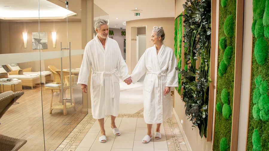 Paar im Bademantel geht Hand in Hand durch den Spa-Flur