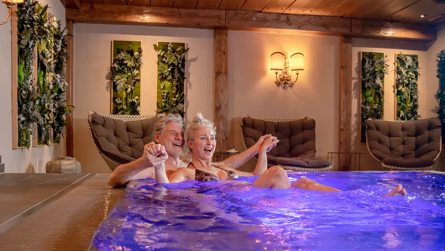 Paar lacht im beleuchteten Whirlpool des Spa-Bereichs