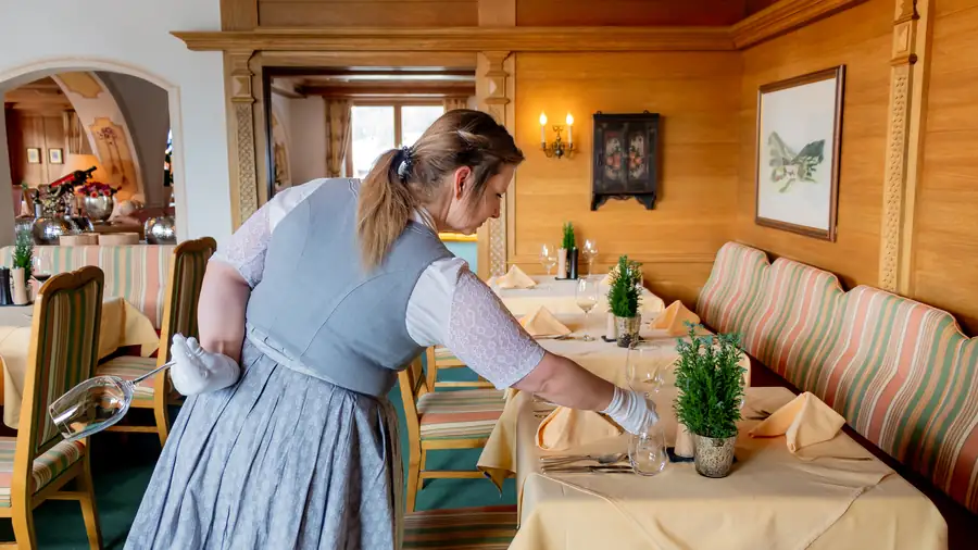 Servicekraft im Dirndl deckt einen Tisch im Restaurant ein