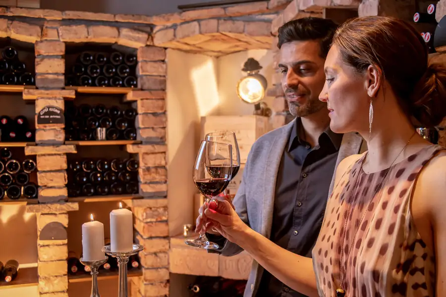 Zwei Gäste prüfen ein Glas Rotwein im Gegenlicht